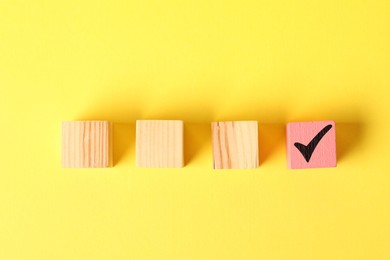 Photo of One pink cube with check mark among others on yellow background, flat lay