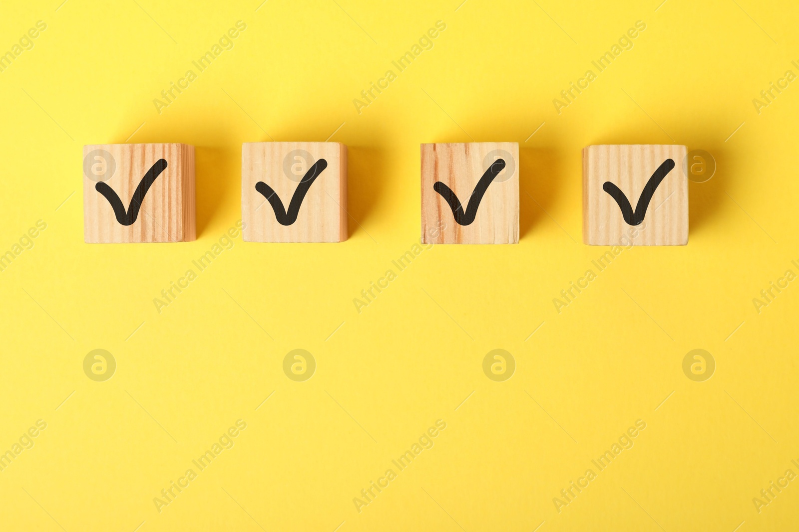 Photo of Wooden cubes with check marks on yellow background, flat lay. Space for text