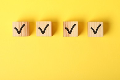 Photo of Wooden cubes with check marks on yellow background, flat lay. Space for text