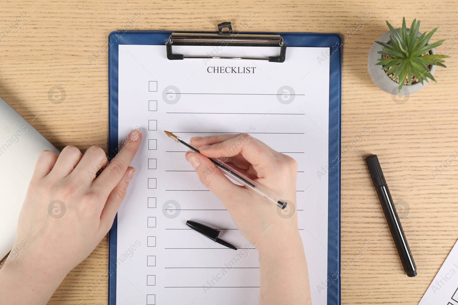 Photo of Woman filling Checklist with pen at wooden table, top view