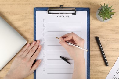 Photo of Woman filling Checklist with pen at wooden table, top view