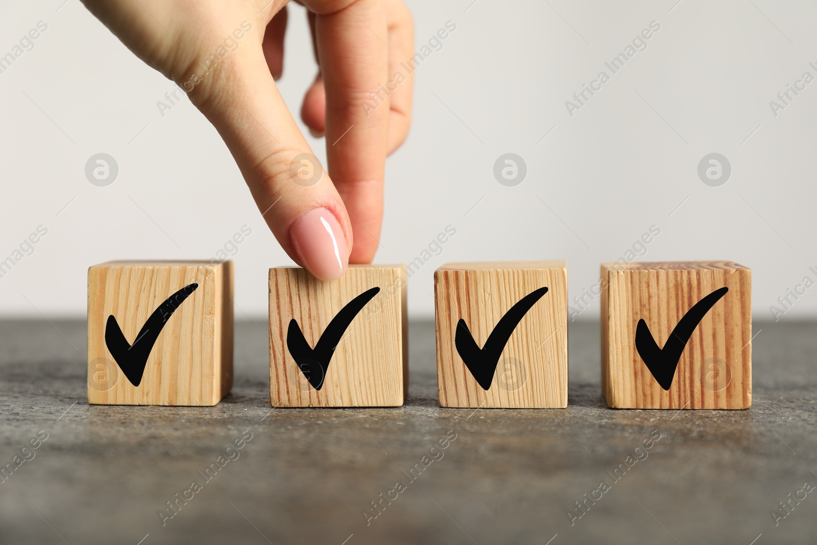 Photo of Woman taking wooden cube with check mark at grey table, closeup