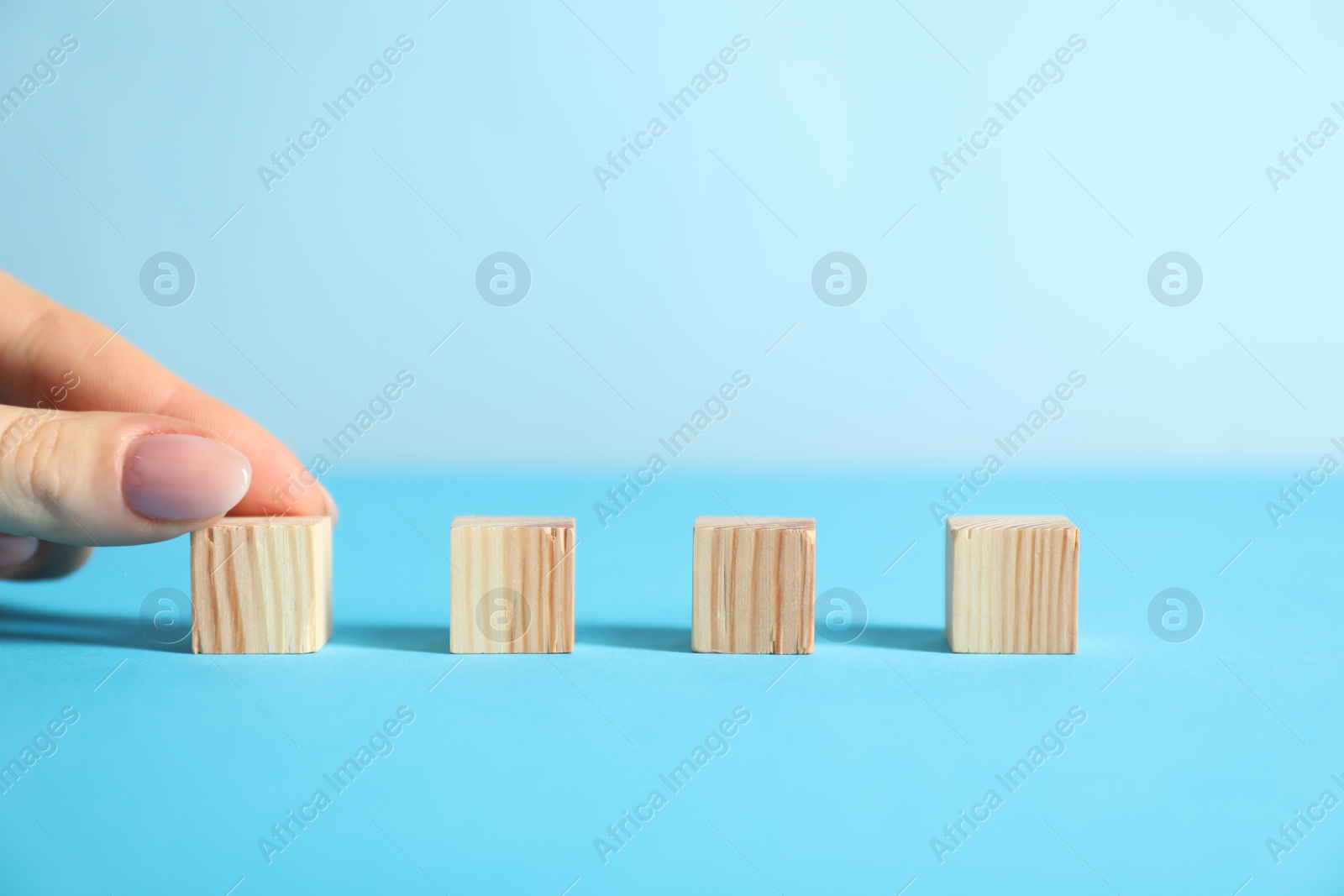 Photo of Woman with wooden cubes on light blue background, closeup