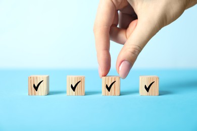 Photo of Woman taking wooden cube with check mark on light blue background, closeup