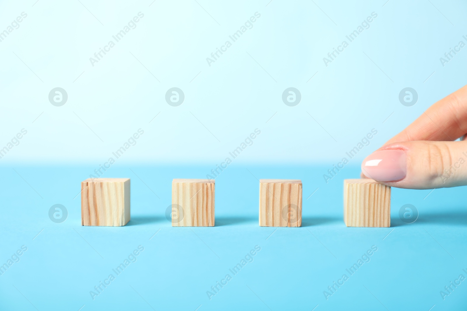 Photo of Woman with wooden cubes on light blue background, closeup