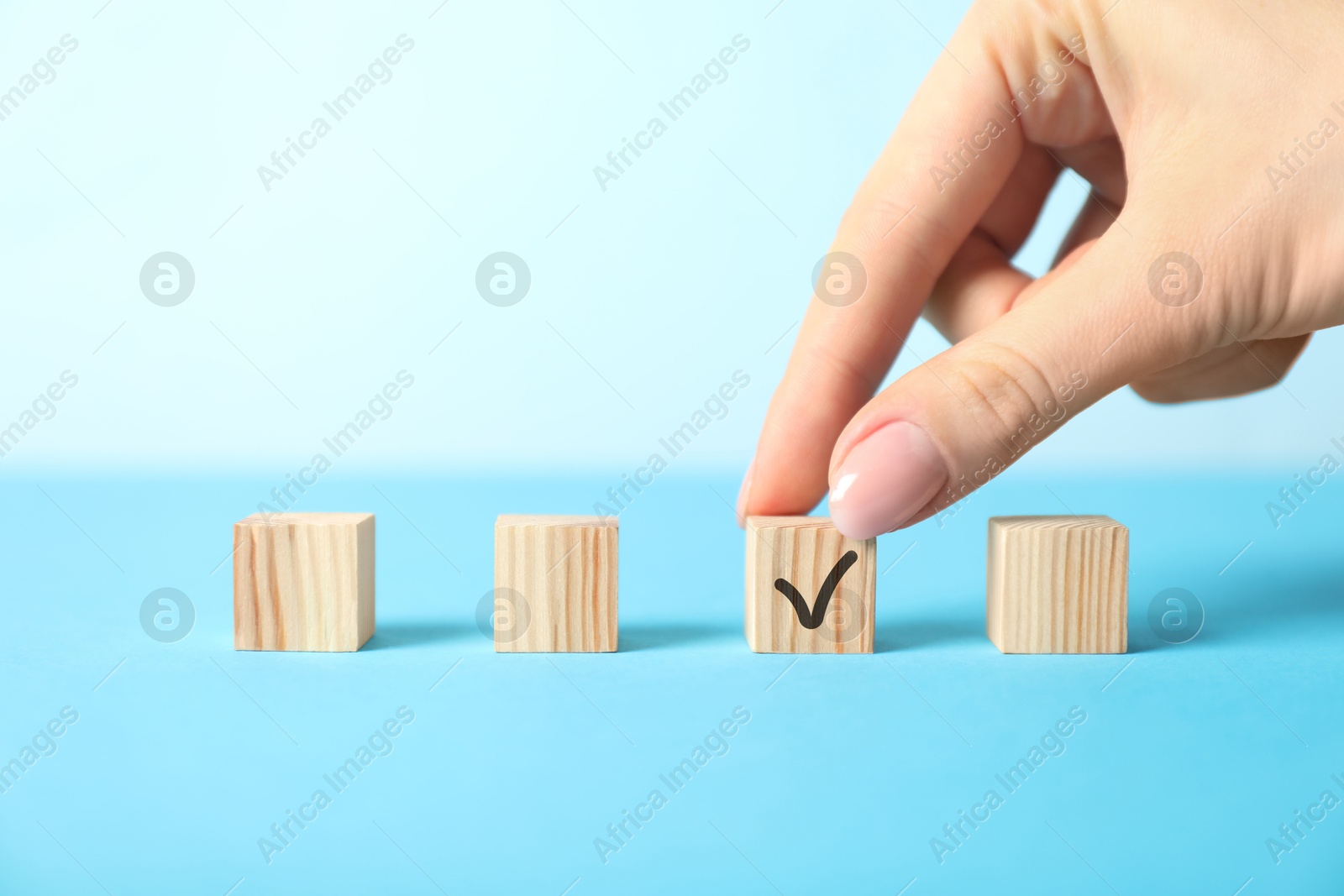 Photo of Woman taking wooden cube with check mark on light blue background, closeup