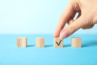 Photo of Woman taking wooden cube with check mark on light blue background, closeup