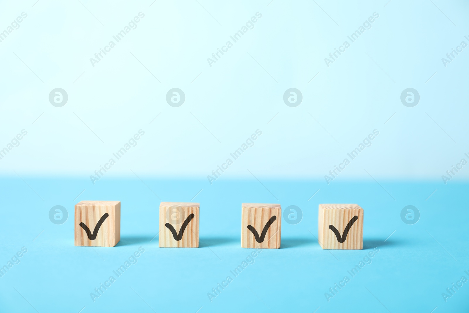 Photo of Wooden cubes with check marks on light blue background, space for text