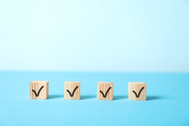 Photo of Wooden cubes with check marks on light blue background, space for text