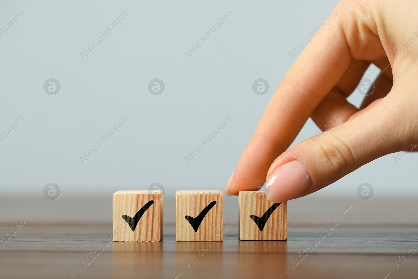 Photo of Woman taking wooden cube with check mark at grey table, closeup