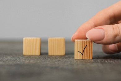 Photo of Woman taking wooden cube with check mark at grey table, closeup