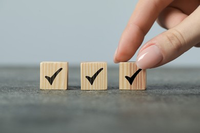 Photo of Woman taking wooden cube with check mark at grey table, closeup