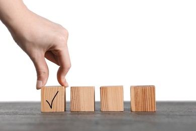 Photo of Woman taking wooden cube with check mark at grey table, closeup