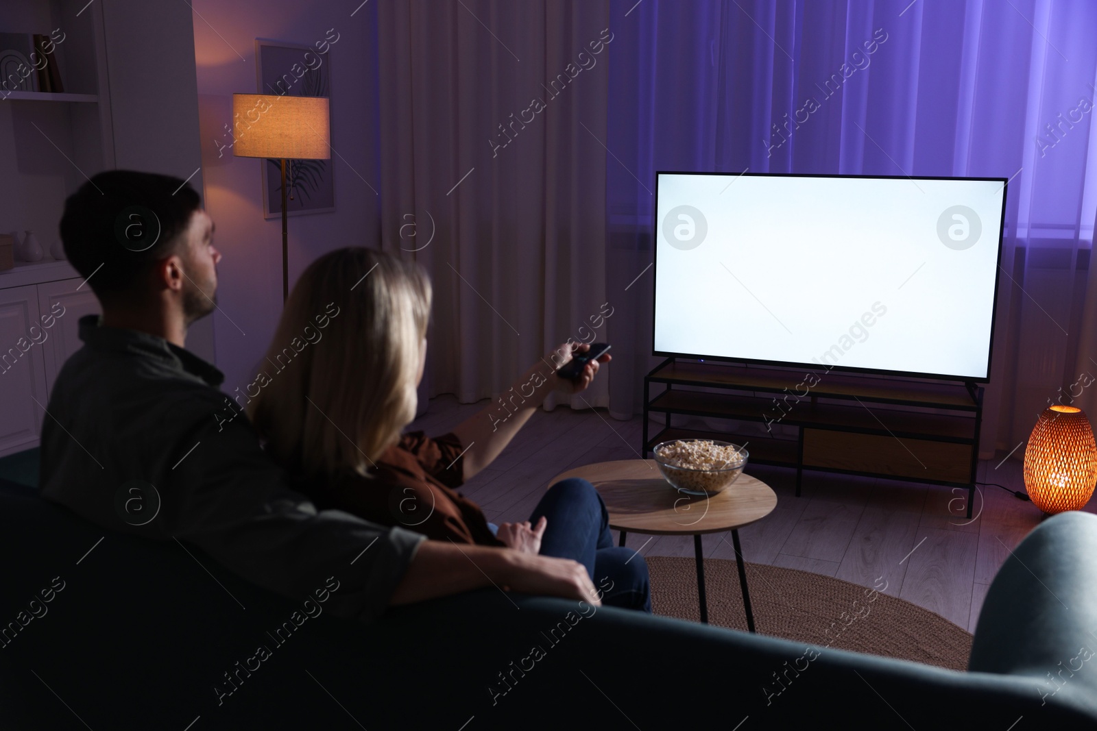 Photo of Lovely couple watching tv at home in evening, back view