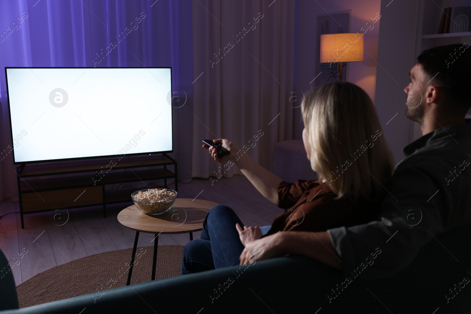 Photo of Lovely couple watching tv at home in evening, back view