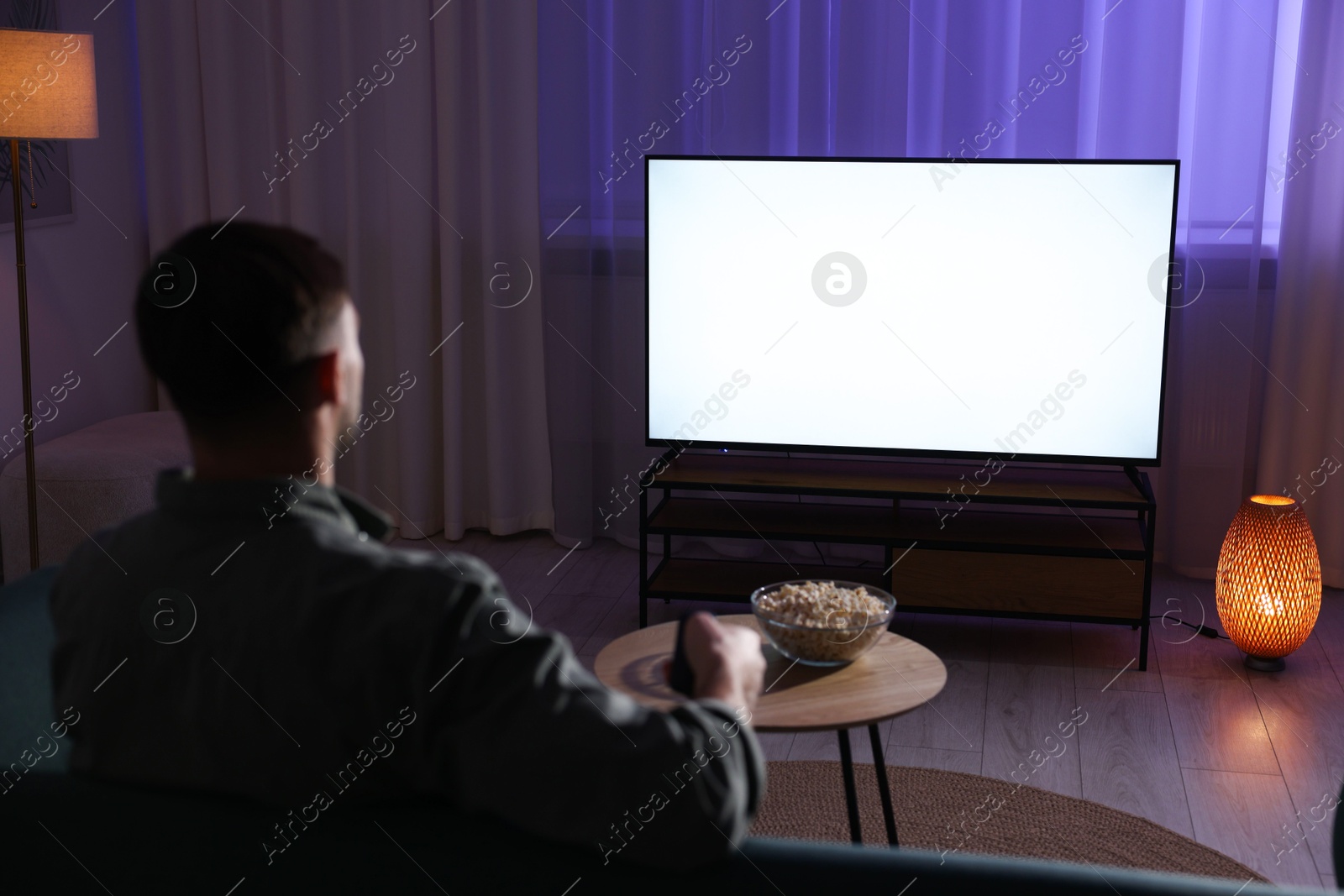 Photo of Man watching tv at home in evening, back view