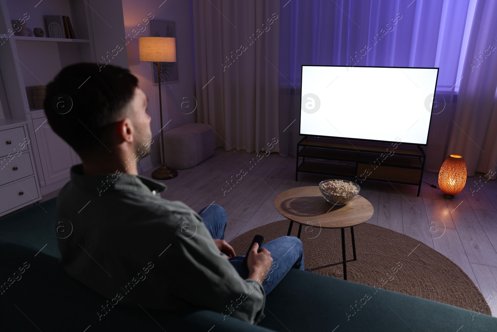 Photo of Man watching tv at home in evening, back view