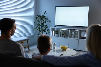 Photo of Happy family with snacks and drinks watching tv together at home, back view