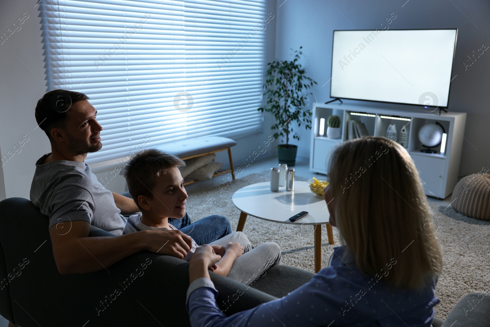 Photo of Happy family with snacks and drinks watching tv together at home