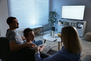 Photo of Happy family with snacks and drinks watching tv together at home