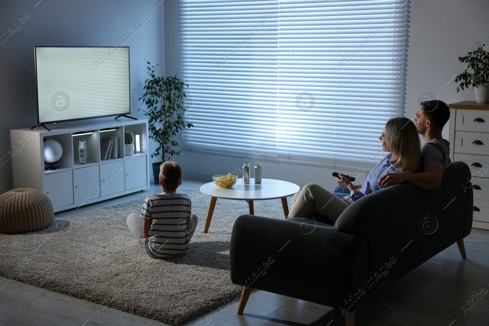 Photo of Happy family with snacks and drinks watching tv together at home