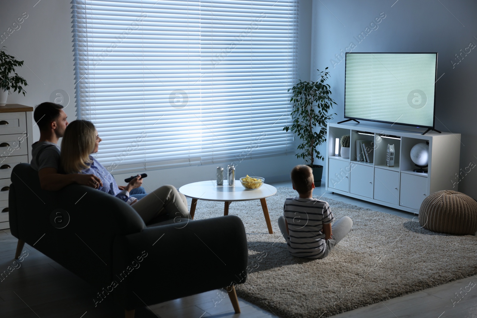 Photo of Happy family with snacks and drinks watching tv together at home