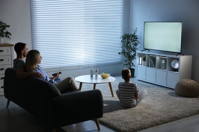 Happy family with snacks and drinks watching tv together at home