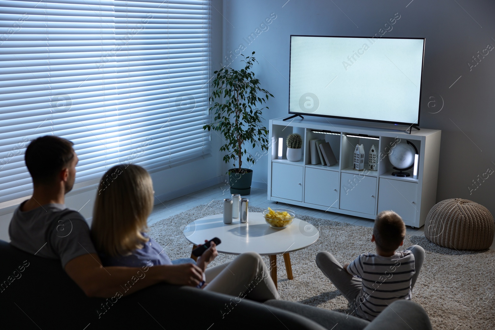 Photo of Happy family with snacks and drinks watching tv together at home