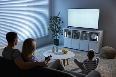 Photo of Happy family with snacks and drinks watching tv together at home