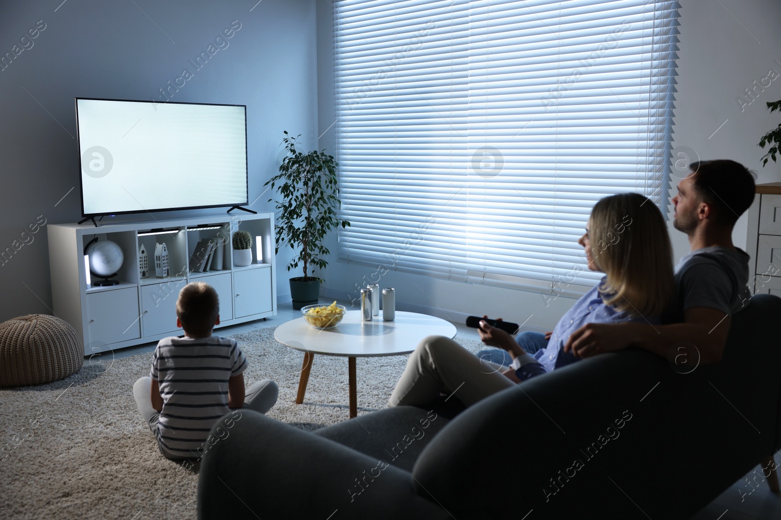 Photo of Happy family with snacks and drinks watching tv together at home