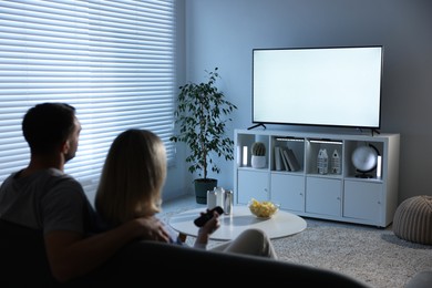 Lovely couple watching tv on couch at home, back view