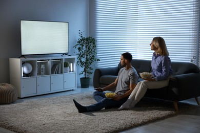 Lovely couple with snacks watching tv at home