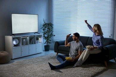 Photo of Lovely couple with snacks cheering while watching tv at home