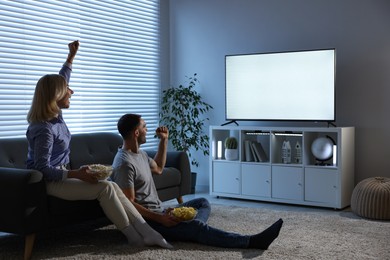 Photo of Lovely couple with snacks cheering while watching tv at home