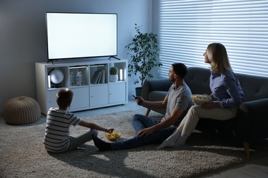 Photo of Happy family with snacks watching tv together at home