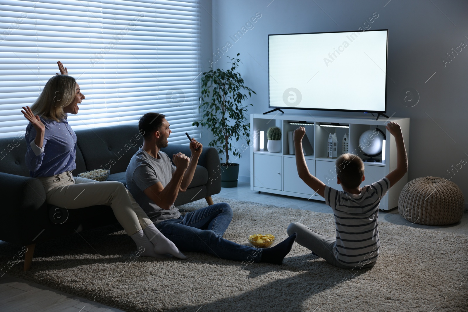 Photo of Happy family with snacks cheering while watching tv together at home