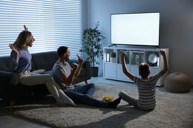 Happy family with snacks cheering while watching tv together at home