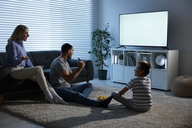 Photo of Happy family with snacks cheering while watching tv together at home