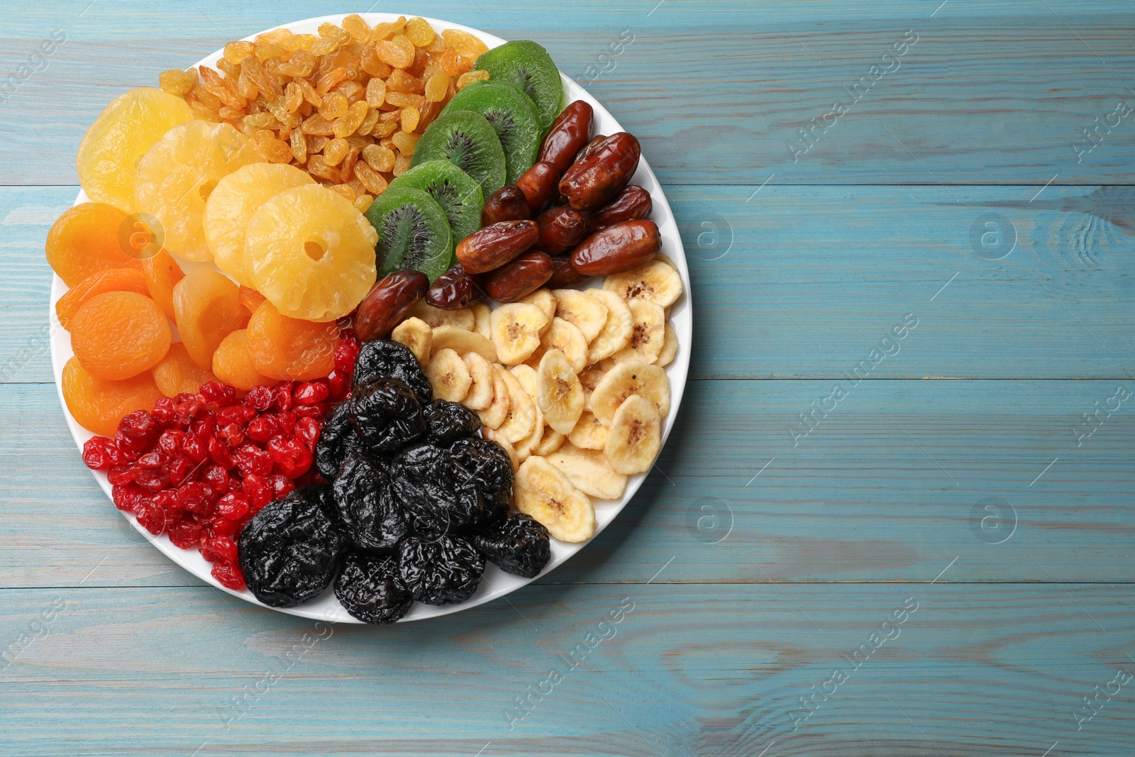 Photo of Mix of different dried fruits on light blue wooden table, top view. Space for text