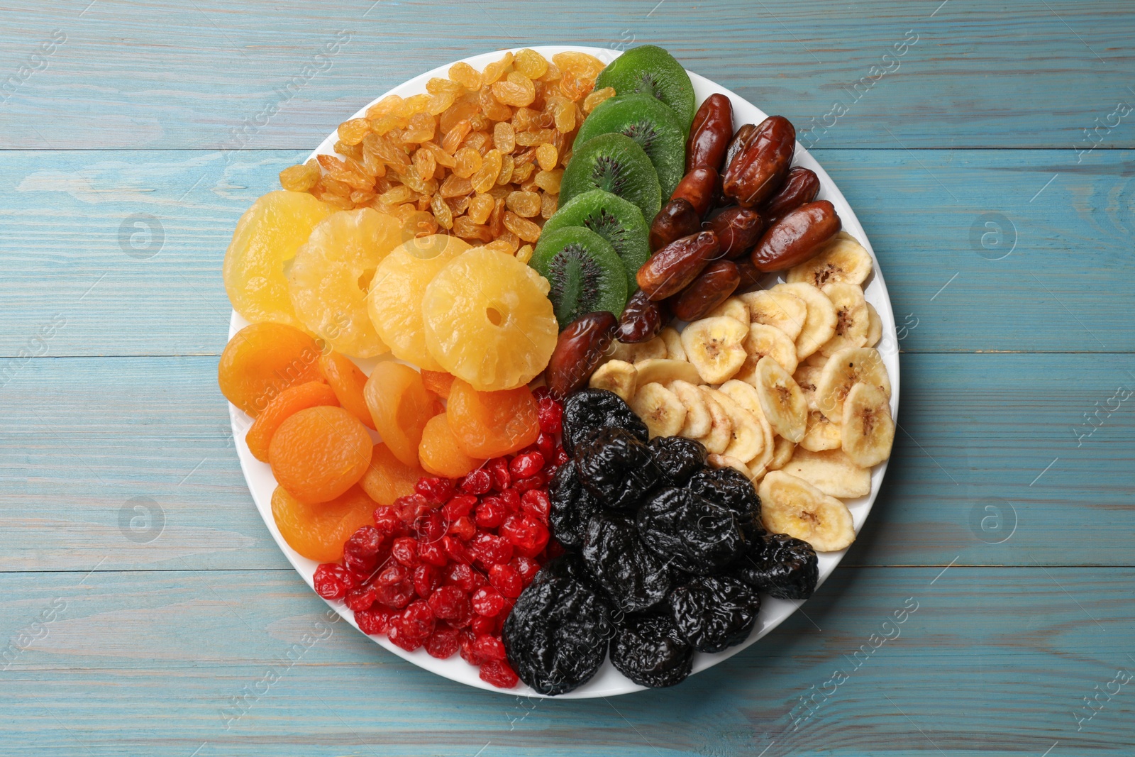 Photo of Mix of different dried fruits on light blue wooden table, top view