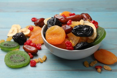 Photo of Mix of different dried fruits in bowl on light blue wooden table, closeup