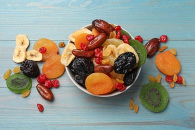 Photo of Mix of different dried fruits in bowl on light blue wooden table, flat lay