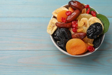 Photo of Mix of different dried fruits in bowl on light blue wooden table, top view. Space for text