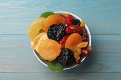 Photo of Mix of different dried fruits in bowl on light blue wooden table, top view