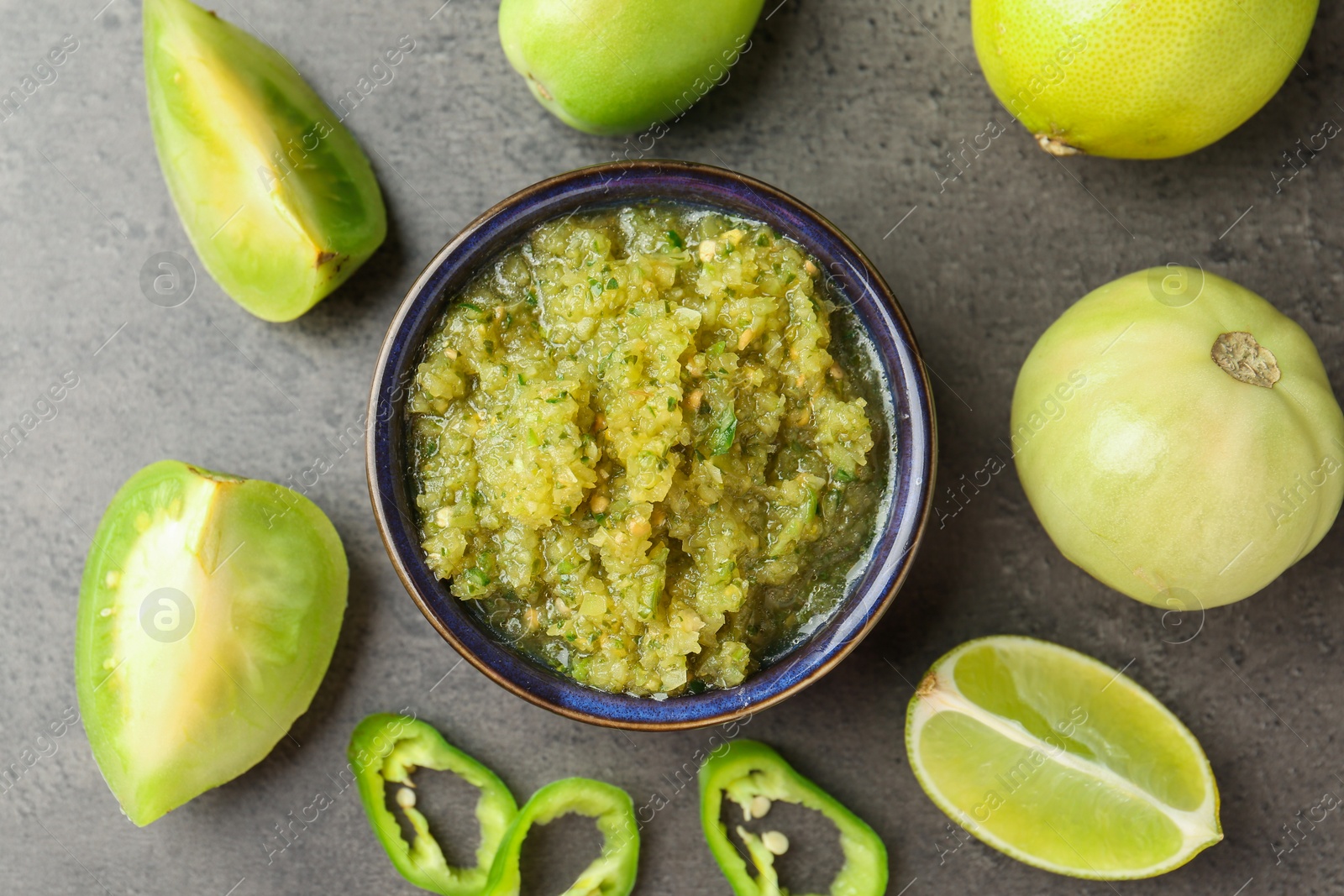 Photo of Delicious salsa sauce in bowl and products on grey textured table, flat lay