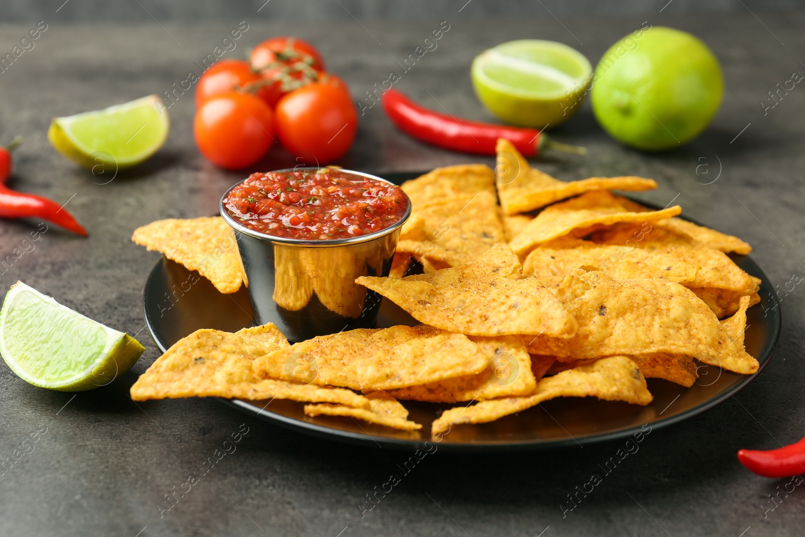 Photo of Delicious salsa sauce served with nachos on grey textured table, closeup