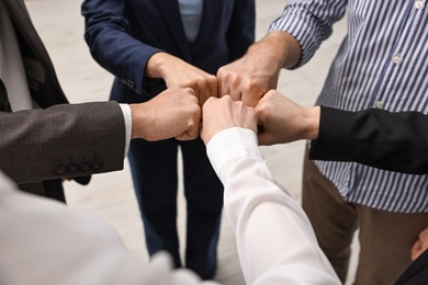 Teamwork. Group of people joining fists together indoors, closeup