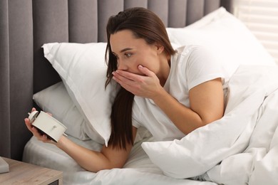 Overslept woman with alarm clock in bed at home