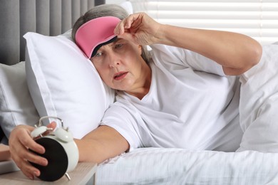 Photo of Overslept woman looking at alarm clock in bed indoors