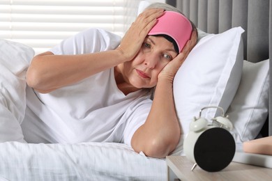 Photo of Overslept woman looking at alarm clock in bed indoors